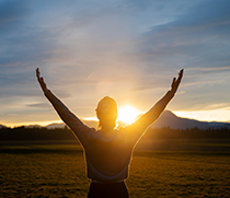 Eine Frau hält streckt die Arme in die Luft vor einem Berg beim Sonnenuntergang